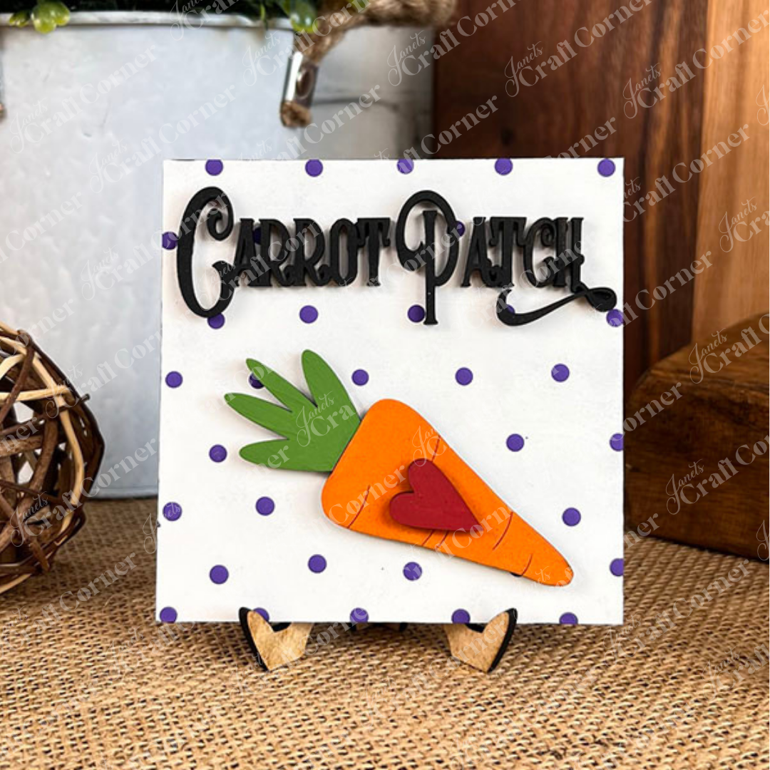 Add festive charm with Janet's Craft Corner Easter Bunny Squares—a swappable sign featuring "Carrot Patch" text, a big cartoon carrot with a red heart, and purple polka dots on white, all on a small wooden easel. Perfect for tiered tray displays!.