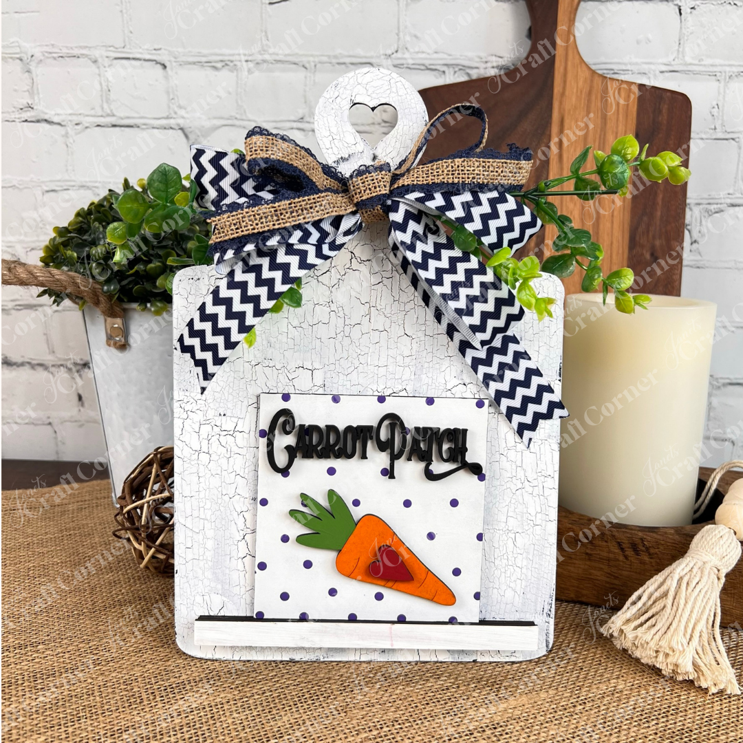 The Easter Bunny Squares by Janet's Craft Corner are decorative white wooden signs with heart cutouts, zigzag bows, greenery, and "Carrot Patch" text—perfect wood cut-outs or tiered tray decor for a rustic table setting.