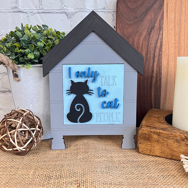 Janet's Craft Corner Cat Swappable Squares feature a house-shaped sign with a black cat silhouette and "I only talk to cat people" in blue—ideal DIY home decor for small spaces, shown with plants, a candle, and wood accents.
