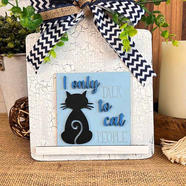 Janet's Craft Corner Cat Swappable Squares: A decorative sign featuring a black cat silhouette and "I only talk to cat people" text, with blue and white chevron ribbons and greenery, ideal DIY seasonal decor for small spaces.