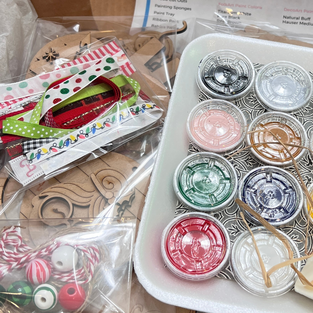 A close-up of craft supplies from Janet's Craft Corner’s Crafted by You! Subscription—paint pots, ribbons, wooden ornaments, and festive twine with beads—all packaged for your July 2025 monthly DIY home decor craft kit.