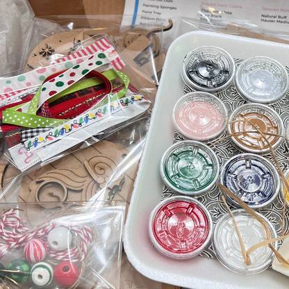 A close-up of craft supplies from Janet's Craft Corner’s Crafted by You! Subscription—paint pots, ribbons, wooden ornaments, and festive twine with beads—all packaged for your July 2025 monthly DIY home decor craft kit.