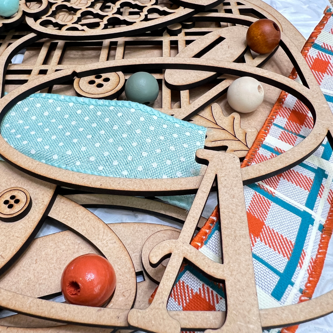A vibrant display of wooden shapes, colorful beads, teal polka-dot fabric, and plaid ribbon from Janet’s Craft Corner’s Crafted by You! Subscription— a monthly DIY home decor craft kit.