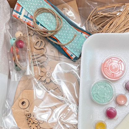 Janet's Craft Corner offers the Crafted by You! Subscription—a DIY home decor craft kit with wooden cutouts, fabric strips, twine, beads, and pastel paints—perfect for joining a creative community each month.