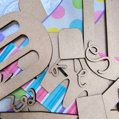 Janet's Craft Corner’s Crafted by You! Subscription features DIY home decor craft kits with wooden letters and shapes, plus colorful ribbons—perfect for playful, vibrant monthly creative projects.