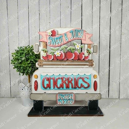 The Cherries Insert from Janet's Craft Corner is a decorative sign shaped like the back of a vintage truck with cherries and banners, plus a potted plant—perfect as a charming DIY seasonal home decor piece against a white wood background.
