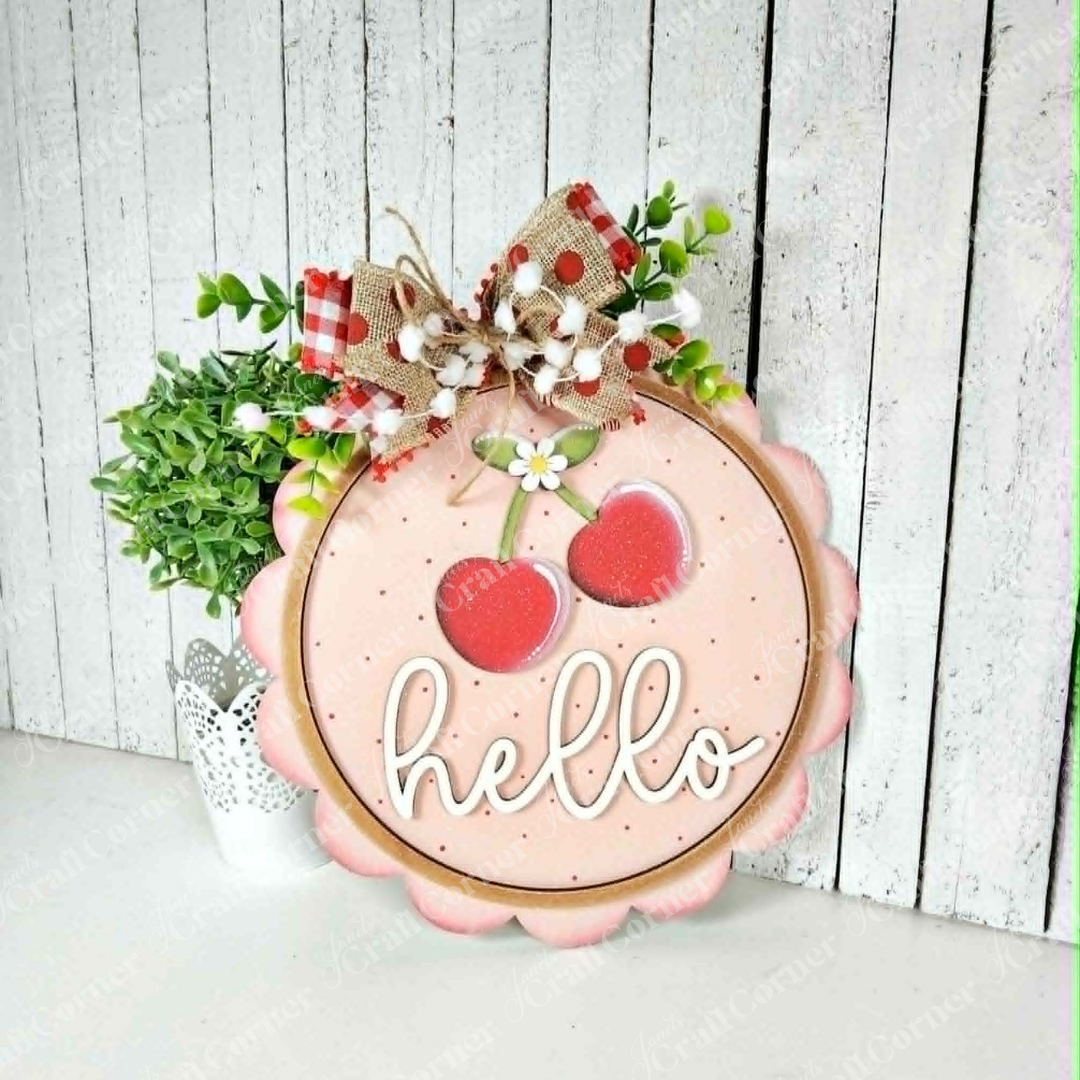 The Janet's Craft Corner Cherry Hello Scallop Door/Wall Hanger is a DIY seasonal home décor craft kit featuring pink wood with cherries, "hello" in white script, and a floral bow. Perfect farmhouse-style accent for your wall or door. Set of 1.