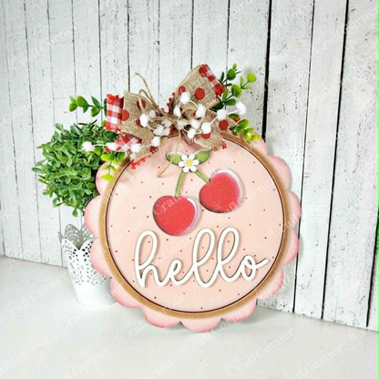 The Janet's Craft Corner Cherry Hello Scallop Door/Wall Hanger is a DIY seasonal home décor craft kit featuring pink wood with cherries, "hello" in white script, and a floral bow. Perfect farmhouse-style accent for your wall or door. Set of 1.