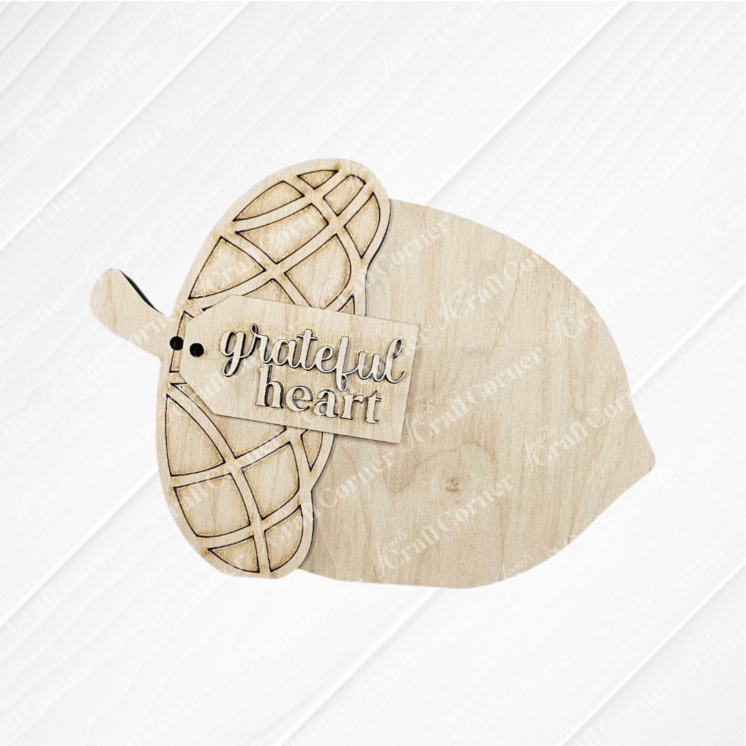 The Fall Chunky Mini Shelf Sitters DIY kit by Janet's Craft Corner features acorn-shaped wooden cutouts with engraved caps and a "grateful heart" sign, perfect for autumn decor on any shelf. Choice of 3 designs available.