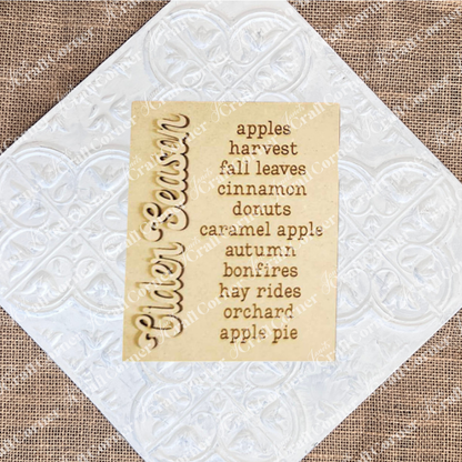 The image beautifully showcases Janet's Craft Corner's "Cider Words Interchangeable Sign" DIY home decor craft kit. The wooden sign, engraved with "Cider Season," is complemented on the right by lively words that evoke apples, harvest, and fall leaves. Together, they conjure the cozy essence of autumn with cinnamon donuts, caramel apple treats, bonfires, hay rides at the orchard, and apple pie delights.