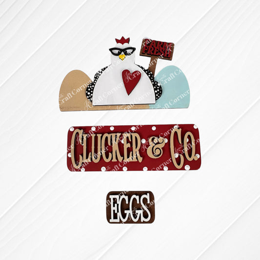 A textured decorative sign set includes a cartoon chicken motif wearing glasses and a "Farm Fresh" sign, accompanied by the illuminated red Clucker & Co. sign by Janet's Craft Corner, which adds rustic charm alongside a brown "Eggs" sign, ideal for interchangeable craft inserts.