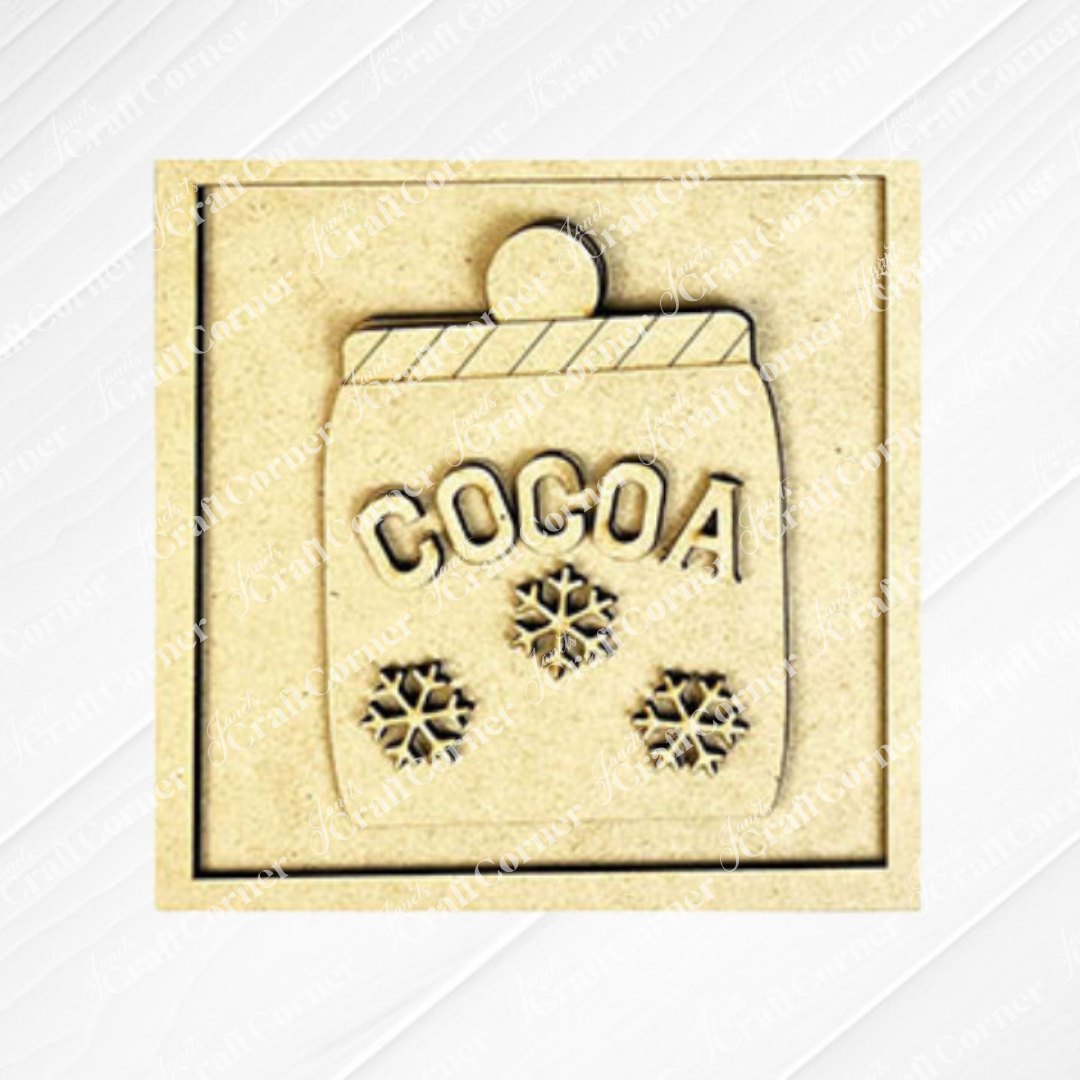 The Hot Cocoa Squares plaque by Janet's Craft Corner is a gold-toned square featuring a "COCOA" mug with a striped rim and three snowflakes, ideal for DIY seasonal home decor.