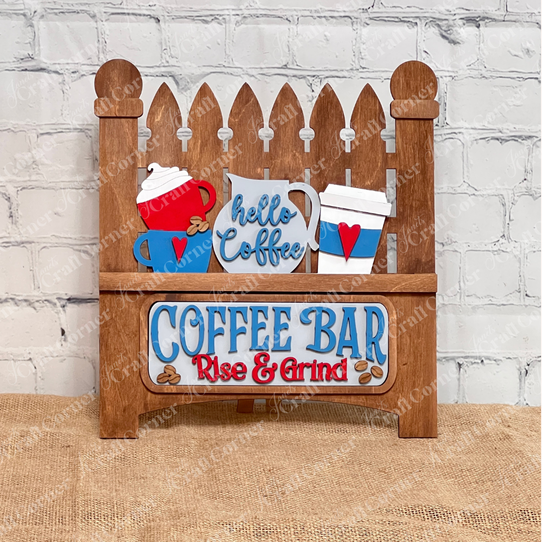 This delightful wooden sign from Janet's Craft Corner, resembling a classic picket fence, showcases coffee-themed designs with cups and a pot. It reads "Hello Coffee" and "COFFEE BAR Rise & Grind," set against a white brick background on burlap, ideal for DIY craft kit enthusiasts.