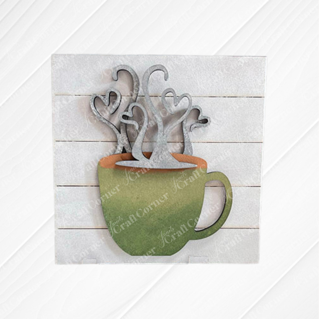 Janet's Craft Corner Coffee Swappable Squares is a DIY seasonal home decor craft kit featuring a wooden coffee mug cutout with heart steam, set on a square slatted background. With a green cup and brown "coffee" it is ideal for coffee lovers and creative projects. 