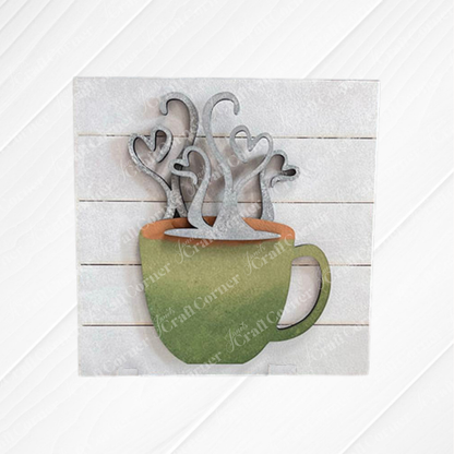 Janet's Craft Corner Coffee Swappable Squares is a DIY seasonal home decor craft kit featuring a wooden coffee mug cutout with heart steam, set on a square slatted background. With a green cup and brown "coffee" it is ideal for coffee lovers and creative projects. 
