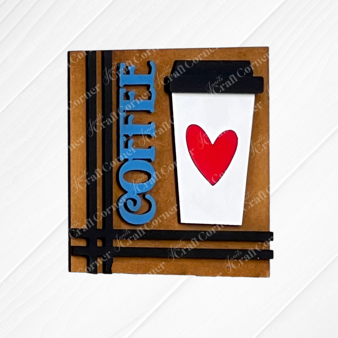 Celebrate coffee lovers with Janet's Craft Corner Coffee Swappable Squares—a DIY seasonal home decor kit featuring a white cup with a red heart, blue "COFFEE" text, and black lid on a white wood. Perfect handmade charm!.
