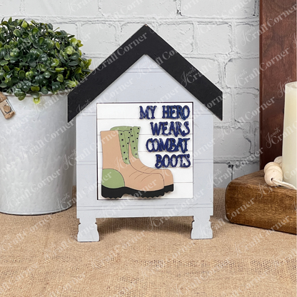 The Military Squares sign from Janet's Craft Corner features a green and tan combat boot with "My Hero Wears Combat Boots." Perfect for tiered tray décor, it’s displayed on burlap beside a potted plant and coiled rope.