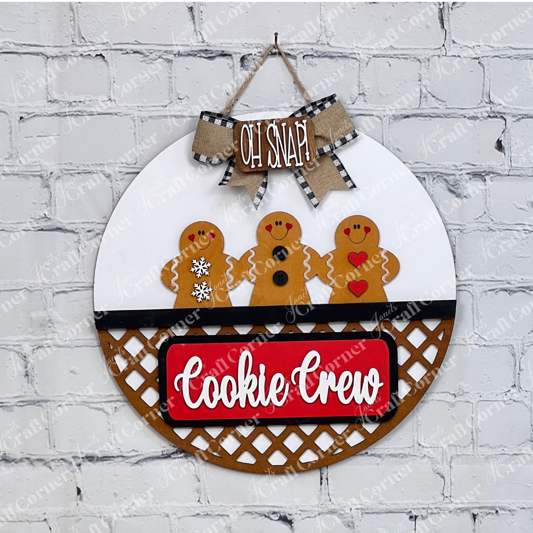 The Cookie Crew Interchangeable Insert by Janet's Craft Corner is a DIY seasonal decor kit with 3 pieces, featuring gingerbread men designs and festive "OH SNAP" and "Cookie Crew" text on a white brick wall background.