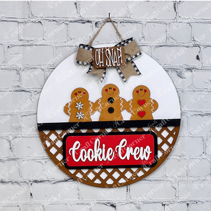 The Cookie Crew Interchangeable Insert by Janet's Craft Corner is a DIY seasonal decor kit with 3 pieces, featuring gingerbread men designs and festive "OH SNAP" and "Cookie Crew" text on a white brick wall background.