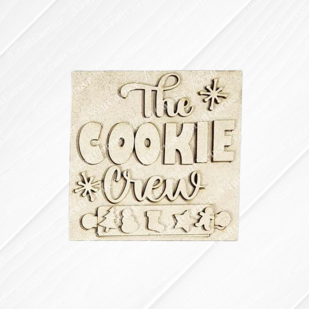 A beige, square sign from Janet's Craft Corner’s Christmas Baking Mini Shelf Sitters kit features raised “The Cookie Crew” text and festive shapes—ideal DIY seasonal decor for your home or Christmas display.