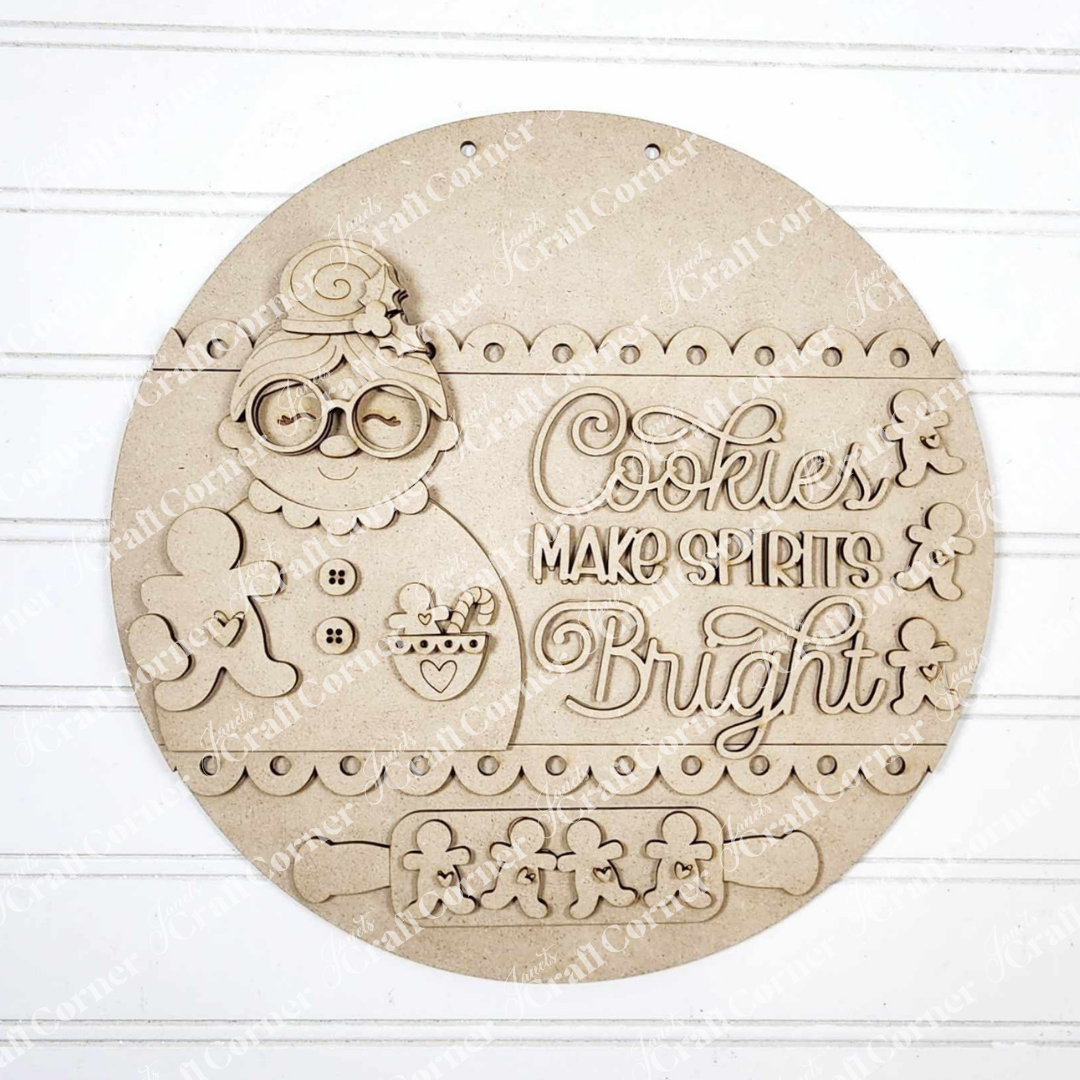 The Cookies Make Spirits Bright Wall Hanger from Janet's Craft Corner is a round wooden DIY kit with an engraved Mrs. Claus, gingerbread cookies, and festive text—perfect for seasonal home decor.