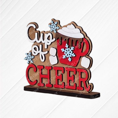 The Hot Cocoa Mini Shelf Sitter from Janet's Craft Corner is a DIY seasonal decor kit featuring "Cup of CHEER" with a red mug, whipped cream, snowflakes, and a mitten handle—perfect cozy home or hot cocoa bar decor. Set of 1.