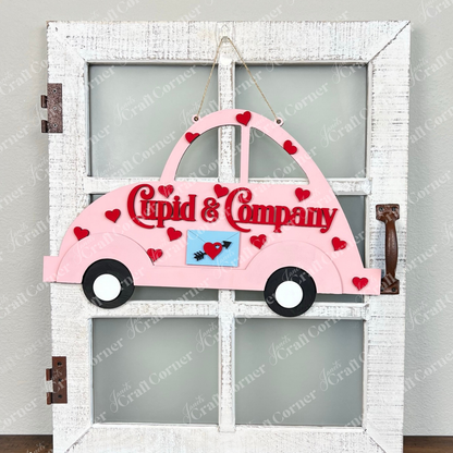 A decorative DIY door hanger from Janet's Craft Corner, in the shape of a pink Cupid Volkswagen, adorns a white door. The sign reads "Cupid & Company" in red letters, embellished with red hearts and an arrow through a heart emblem on the side—perfect for adding charm to your home décor kit.