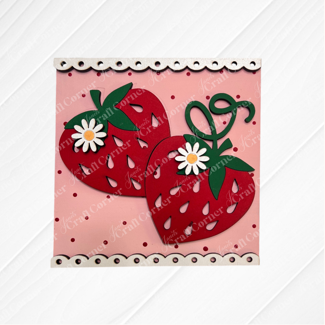 Two large strawberries with green leaves and white daisies rest on a pink polka-dot square with a scalloped edge. Janet's Craft Corner's Strawberry Swappable Squares DIY kit is perfect for seasonal home decor or tray displays.