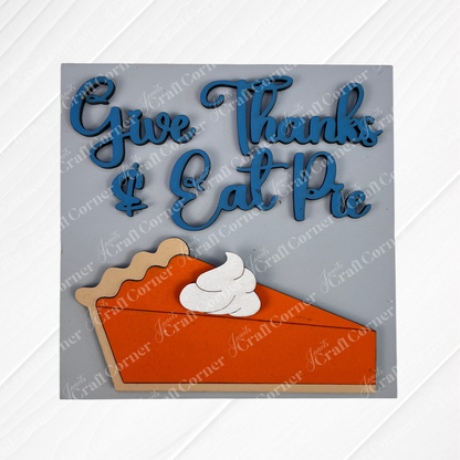 Janet's Craft Corner "Thanksgiving Feast Squares" is a decorative wood cut-out sign featuring "Give Thanks & Eat Pie" in blue above a pumpkin pie, perfect for tiered tray decor.