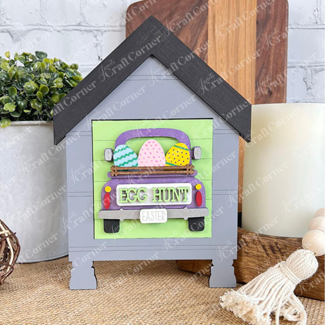 Janet's Craft Corner's Hello Easter Squares is a decorative house-shaped sign with a purple truck carrying colorful Easter eggs and a yellow "Egg Hunt" sign, perfect for coffee-themed decor displays.