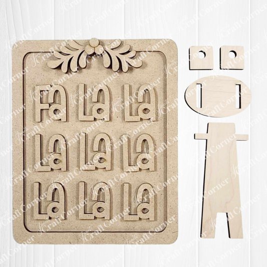 The Fa La La Shelf Sitter DIY craft kit from Janet's Craft Corner includes cut-out pieces, festive accents, and a stand—perfect for creating seasonal home decor. Set of 1, shown on a white wood background.