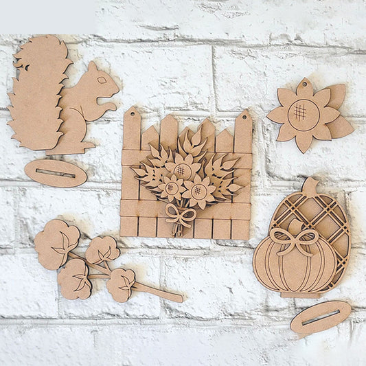 A textured white brick background sets the stage for the **Fall Floral Decor Set - 5 pieces DIY Home Decor Kit** by Janet's Craft Corner, which includes hand-painted wooden cutouts of autumn-themed shapes like a squirrel, sunflowers on a fence, and a pumpkin with a bow. This craft kit allows you to design personalized home décor featuring flowers and sunflower blossoms.