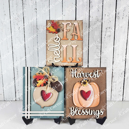 Janet's Craft Corner Fall Switchable Farmhouse Sign—DIY seasonal home décor kit—features raised letters and fall accents. Choose from 9 designs like “Hello FALL” or “Harvest Blessings” on a white wood background with a black stand. Set of 1.