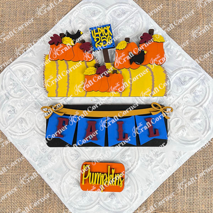 A set of beautifully decorated cookies displayed on a woven mat captures the essence of fall décor with designs featuring pumpkins, hay bales, and crows. One cookie displays the message "4-Pick 5 for 25¢" in a cozy autumn atmosphere, perfectly embodying the style of Janet's Craft Corner's Fall Hay Bale Interchangeable Insert - Painted. This scene brings an interchangeable home decor touch to your seasonal festivities.