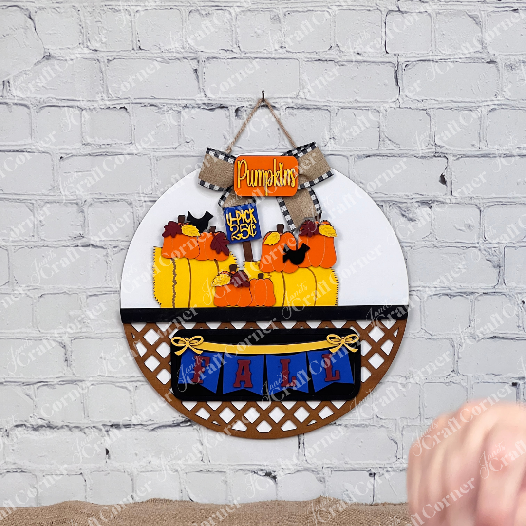 Decorative door hanger with pumpkins and 'Fall' text on a white brick wall background