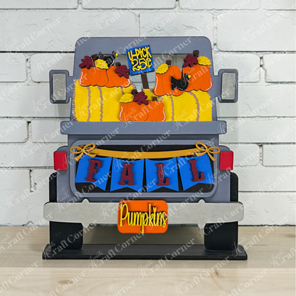 The Off Road Truck Interchangeable Base DIY home decor craft kit set from Janet’s Craft Corner features a gray off-road truck filled with pumpkins, hay bales, and autumn leaves for a charming farmhouse seasonal display. Decorative signs read “FALL,” “Pumpkins,” and “Pick 25¢,” and the truck is set against a white brick wall.