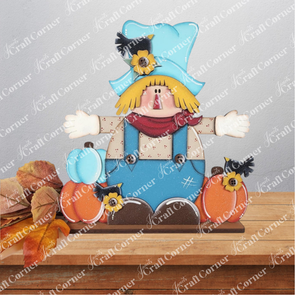 The Fall Scarecrow Shelf Sitter DIY craft kit by Janet's Craft Corner features a cute scarecrow with a blue hat and overalls, surrounded by pumpkins and autumn leaves—perfect seasonal decor for any shelf. Set of 1.