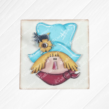 The Fall Scarecrow Squares by Janet's Craft Corner feature a cheerful scarecrow face with a blue hat, yellow hair, flower accent, and red bandana—ideal for autumn home decor or your DIY craft kit.