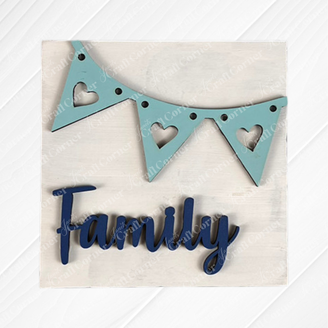 The Family Home Squares sign from Janet's Craft Corner features "Family" in blue script, a light blue heart-accented pennant banner, and a white wood background—ideal for tiered tray decor.