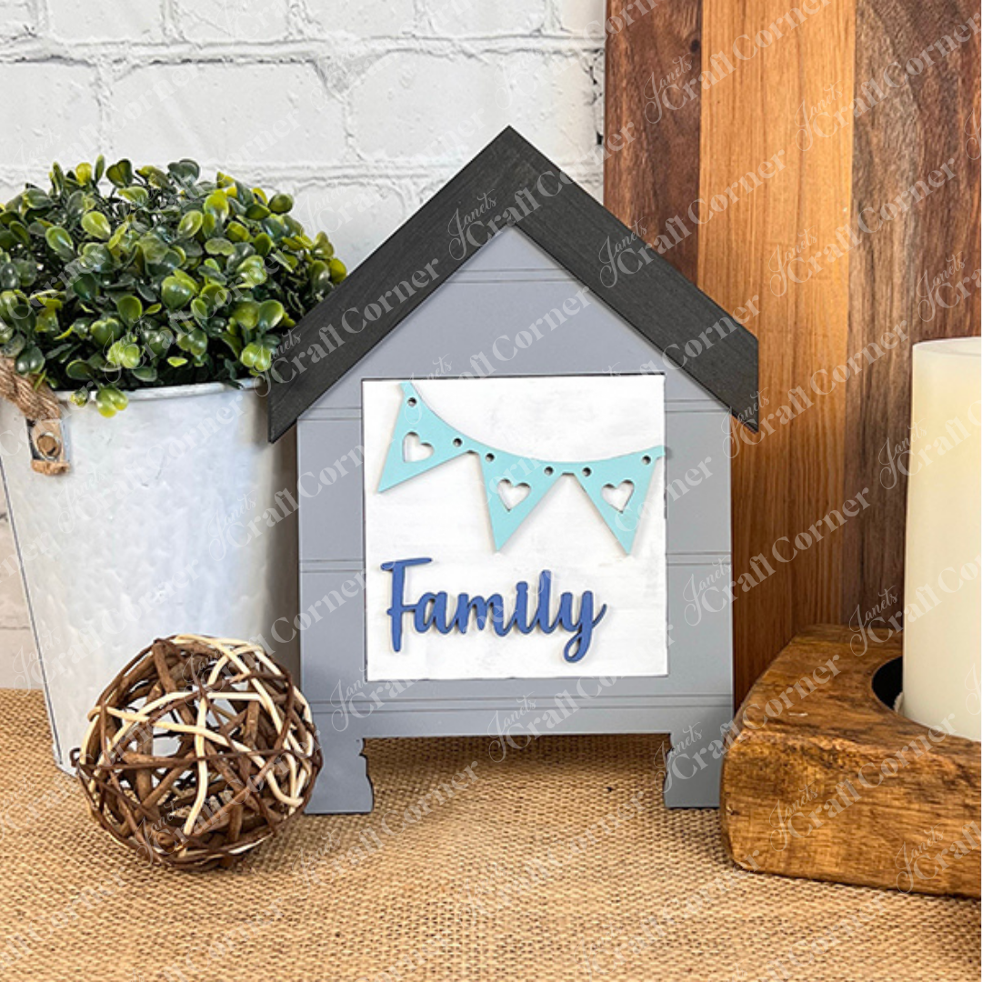 Janet's Craft Corner "Family Home Squares" is a decorative house-shaped wood cut-out sign with "Family" and a blue heart banner—perfect for tiered tray decor on your table next to plants or candles.