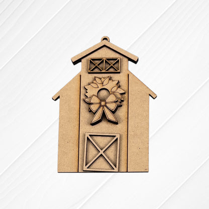 The Farm Life Christmas Ornaments DIY kit by Janet's Craft Corner features a barn-shaped design with a wreath, bow, and X-pattern door on a white textured background. Choose from 4 seasonal ornament styles to craft yourself!.