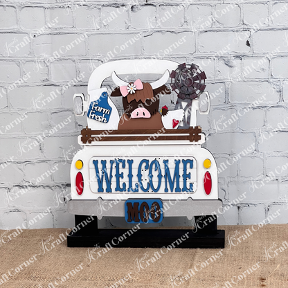The Farm Welcome Interchangeable Insert by Janet's Craft Corner is a DIY home decor craft kit that includes three pieces: a decorative sign shaped like a truck with "WELCOME" and "MOO," featuring a Highland cow with flowers on its head holding a "Farm Fresh" sign against a brick wall backdrop. Perfect for enthusiasts.