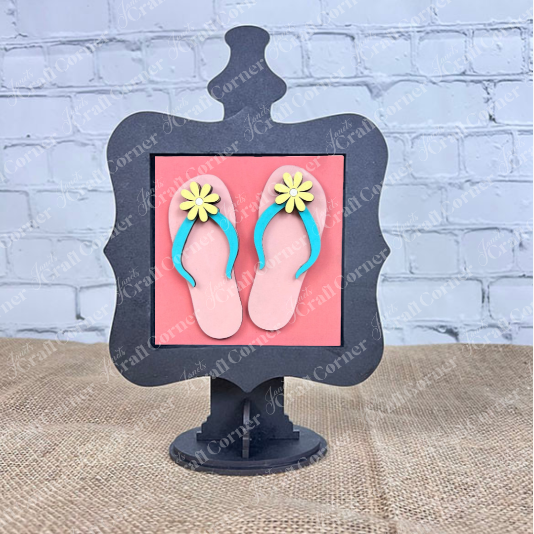 Janet's Craft Corner’s Summer Lovin Swappable Squares DIY kit features a framed pink square with pink flip-flops, yellow daisies, and blue straps—perfect for tiered tray decor on any burlap or white brick background.