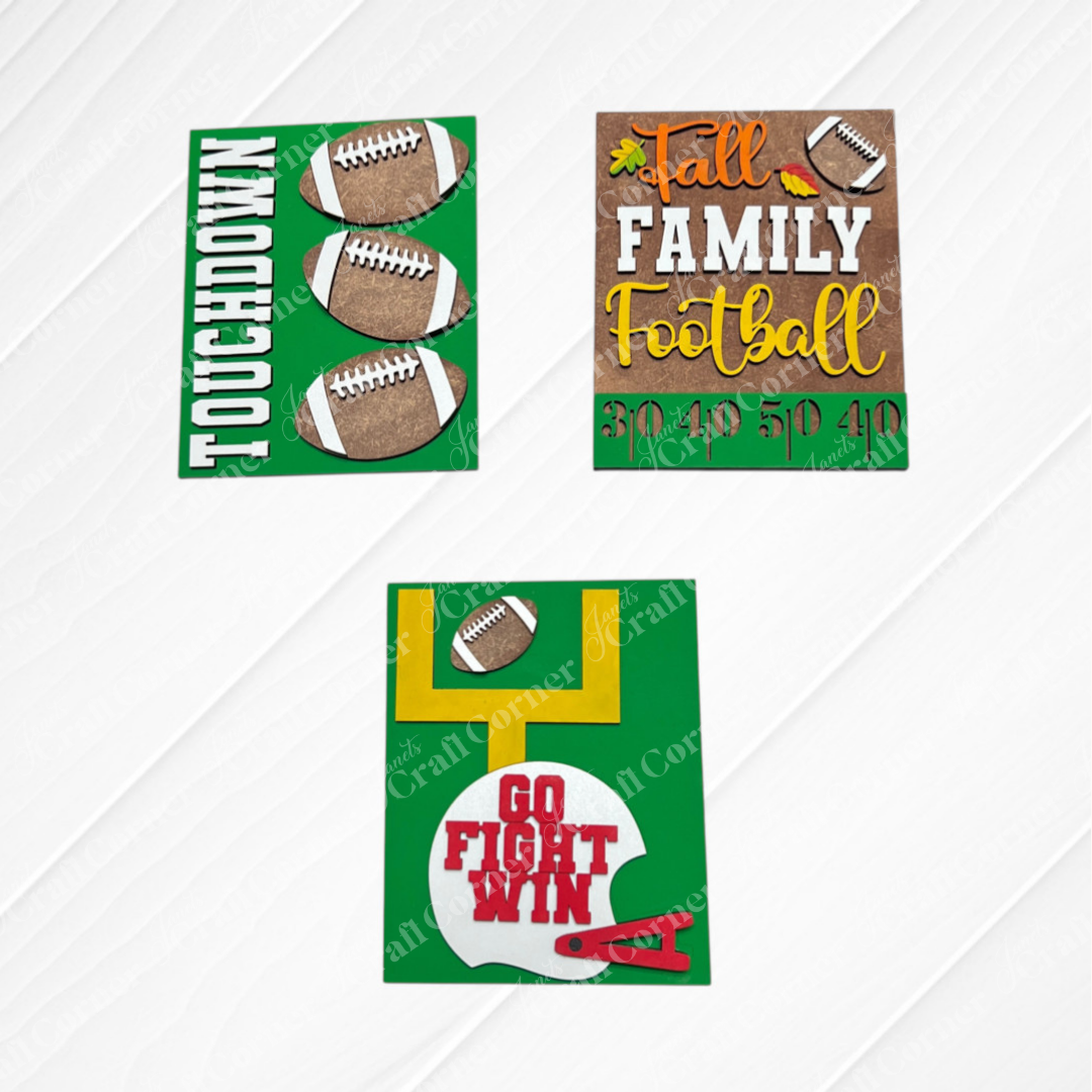 Three “Football Farmhouse Signs” by Janet’s Craft Corner displayed on a white wood background. These cards showcase footballs, goalposts, and phrases such as “TOUCHDOWN,” “FAMILY Football,” and “GO FIGHT WIN” in green, yellow, and red—perfect for interchangeable seasonal decor or as part of your DIY home decor kit.