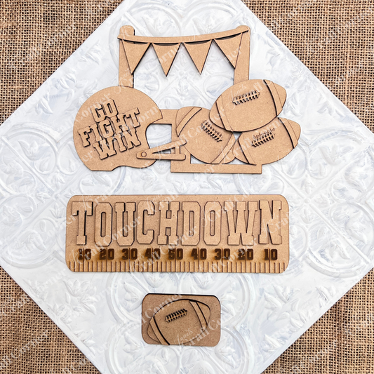 Transform your space with Janet's Craft Corner's Football Interchangeable Insert DIY home decor kit. This hand-painted set features wooden cutouts, including a football helmet inscribed with "Go Fight Win," four footballs, and a “Touchdown” sign above a yard line. It also comes with an additional smaller football insert at the bottom – perfect for adding a personalized touch to your decor.