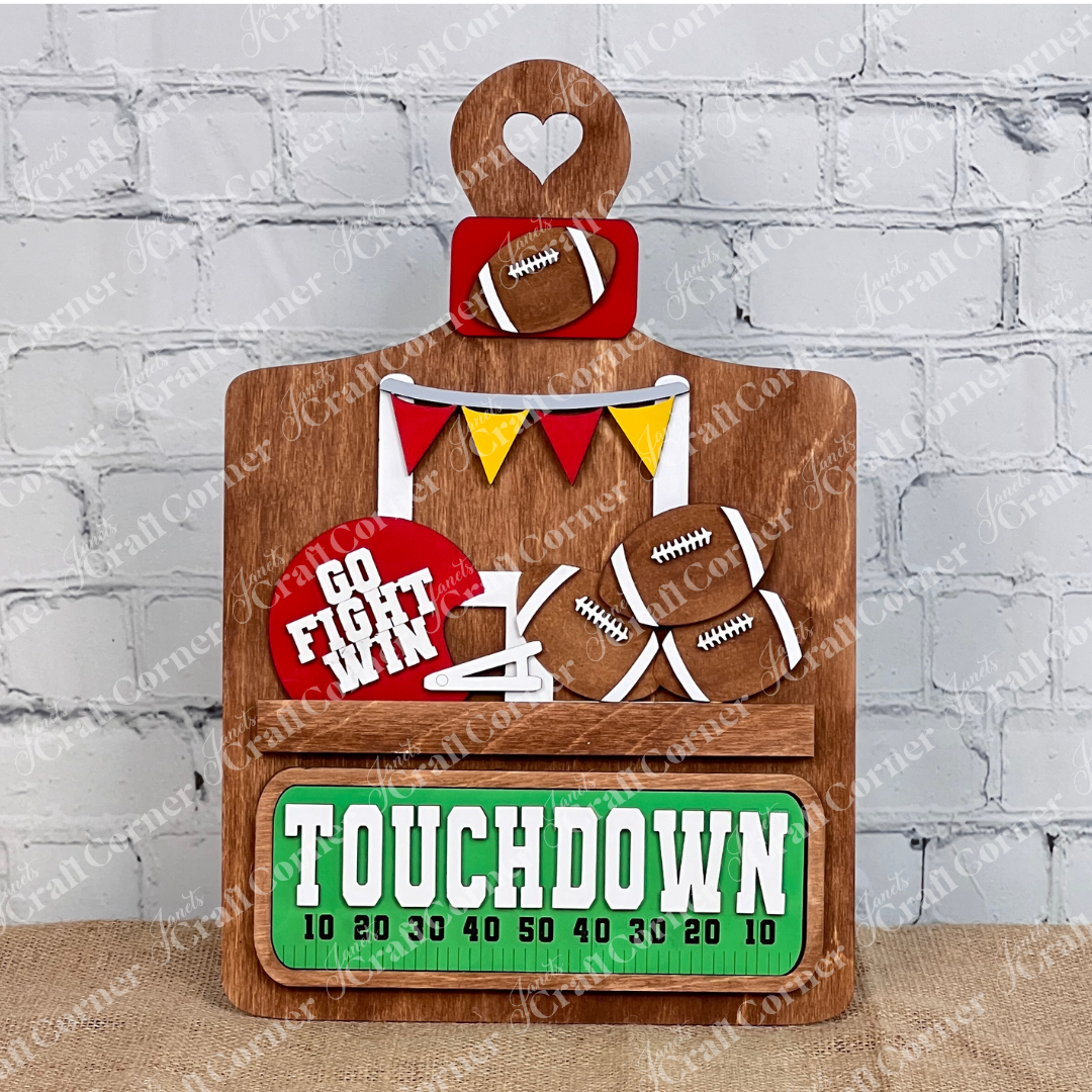 The Breadboard Interchangeable Base with Insert by Janet's Craft Corner offers a wooden football-themed DIY decor kit featuring a "TOUCHDOWN" scoreboard, mini footballs, colorful banners, and "GO FIGHT WIN" on red. Perfect for rustic charm against white brick and burlap surfaces.