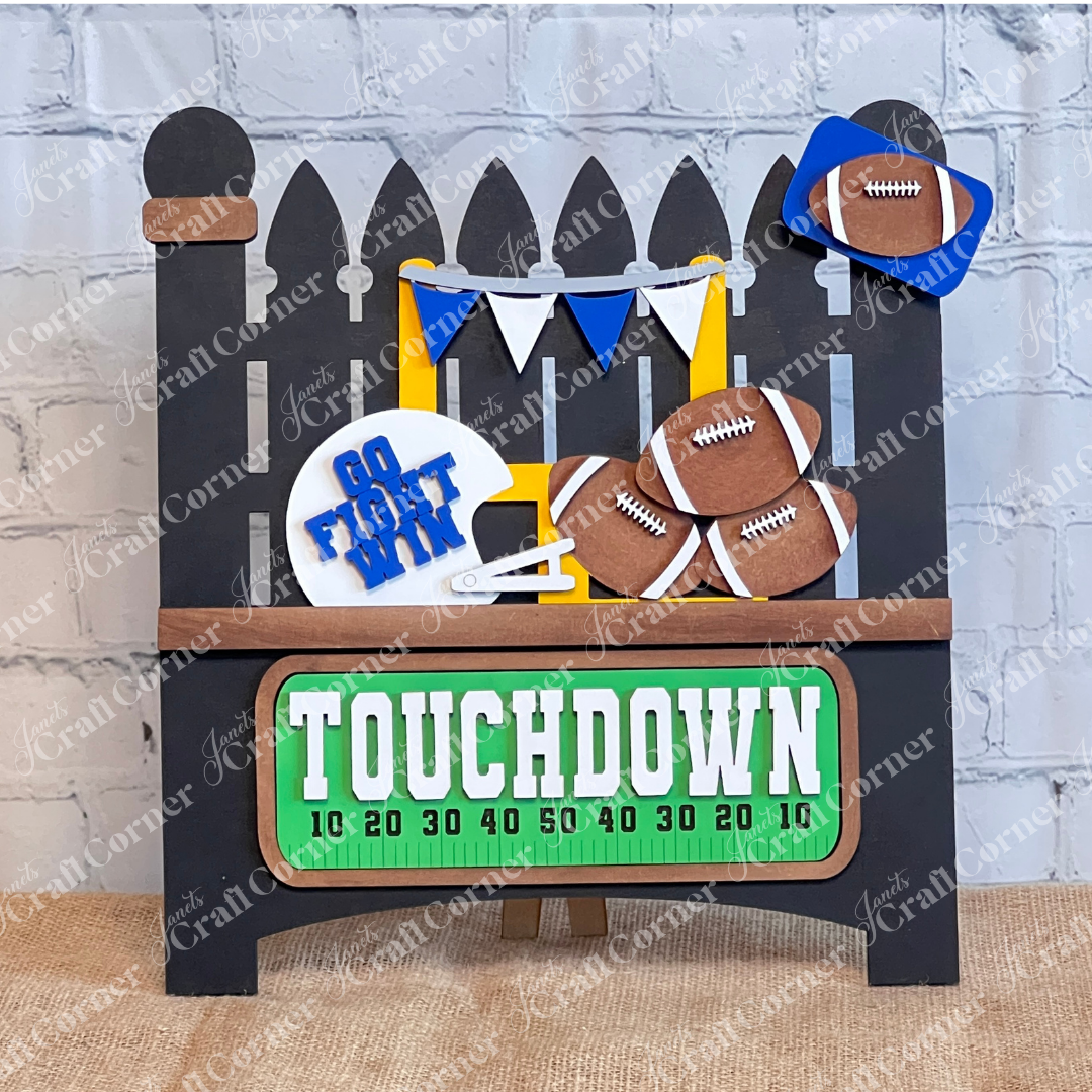 Introducing the Football Interchangeable Insert DIY home decor kit by Janet's Craft Corner: This adorable garden fence set showcases football-themed blue & white accents, including interchangeable footballs, helmets with "Go Fight Win," a goalpost, and a "Touchdown" sign. Perfectly set against a white brick wall backdrop, it offers an ideal project for hand-painted DIY craft enthusiasts looking to add a personal touch to their decor.