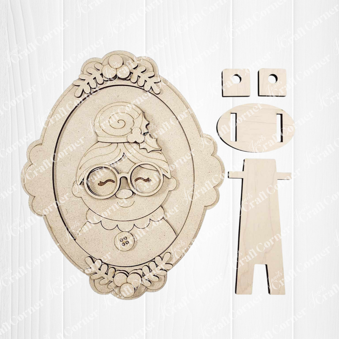 Janet's Craft Corner Framed Mrs. Claus Shelf Sitter: an oval, laser-cut wooden portrait of a smiling elderly woman with glasses and a bun, includes separate stand pieces—perfect DIY kit for charming holiday home decor.