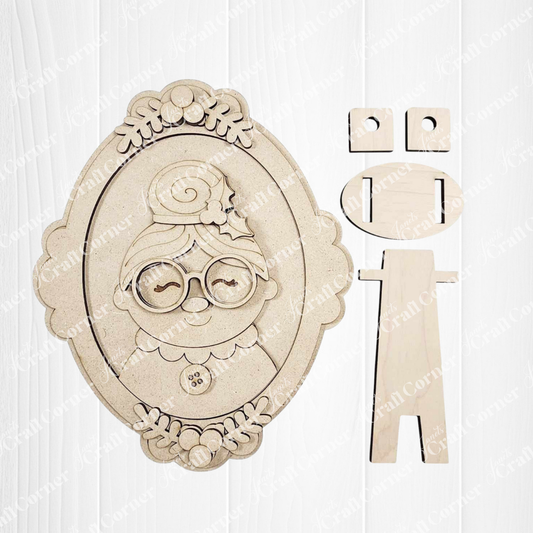Janet's Craft Corner Framed Mrs. Claus Shelf Sitter: an oval, laser-cut wooden portrait of a smiling elderly woman with glasses and a bun, includes separate stand pieces—perfect DIY kit for charming holiday home decor.