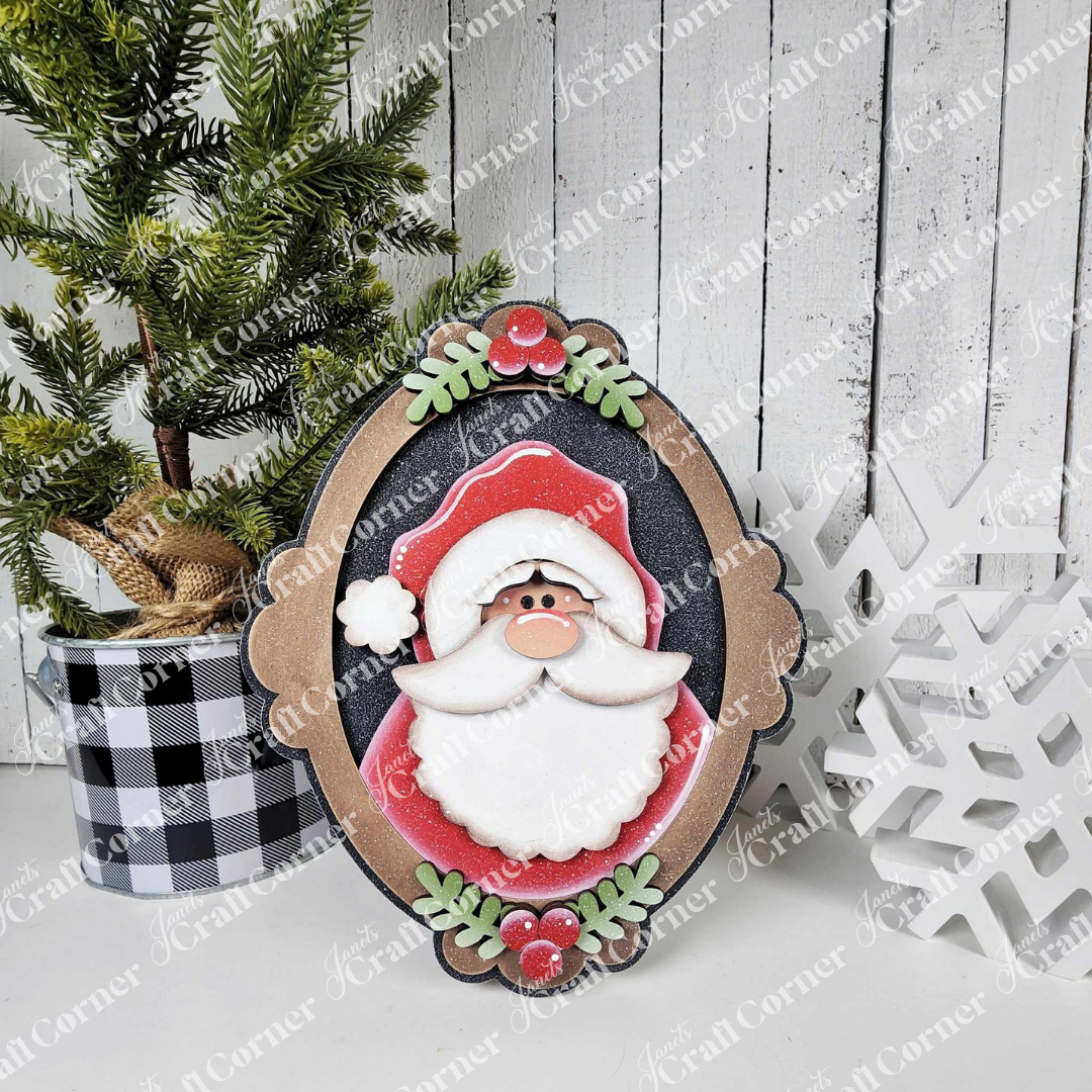 A festive scene features a potted pine, Janet's Craft Corner Framed Santa Shelf Sitter, and a white snowflake ornament on a white wooden surface with a plaid pot—perfect for charming seasonal home decor.